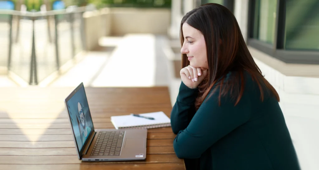 A woman attending an online therapy session on a laptop at an outdoor table
